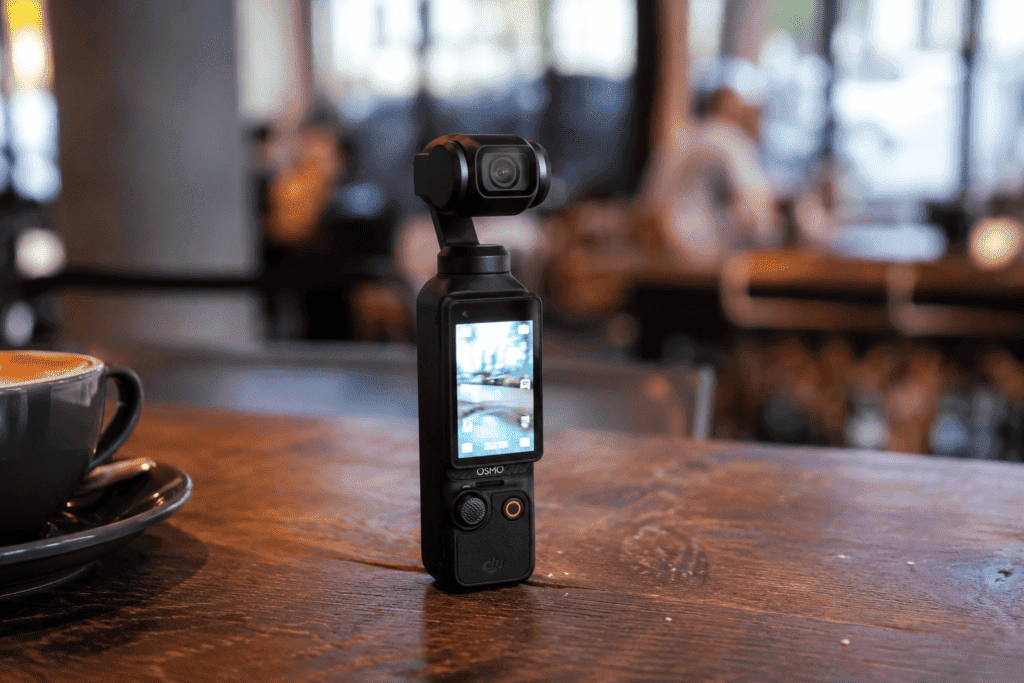 The DJI Osmo Pocket 4 handheld gimbal camera resting on a wooden desk next to a smartphone.