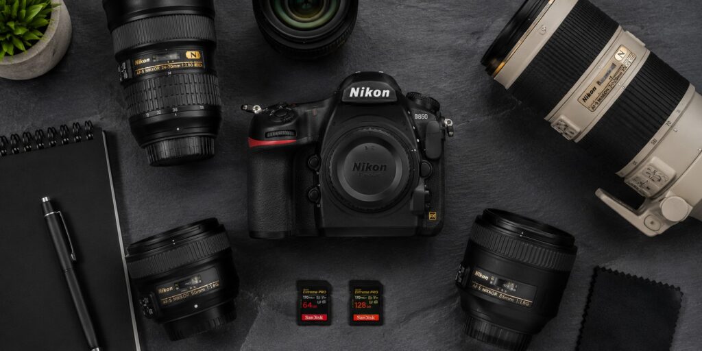 Flat lay overhead view of Nikon D850 camera surrounded by F-mount lenses and photography accessories on a slate surface