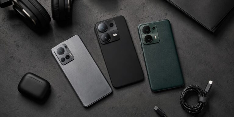 Top-down view of three premium smartphones with metal, matte, and leather finishes arranged neatly on a dark concrete desk with tech accessories.