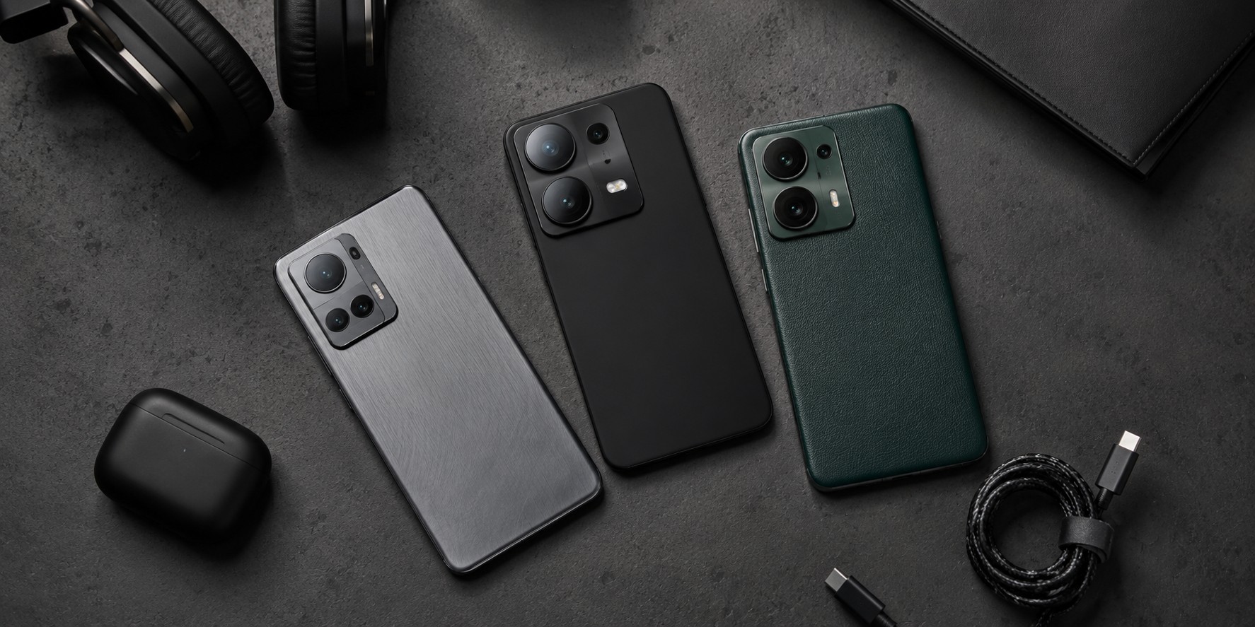 Top-down view of three premium smartphones with metal, matte, and leather finishes arranged neatly on a dark concrete desk with tech accessories.